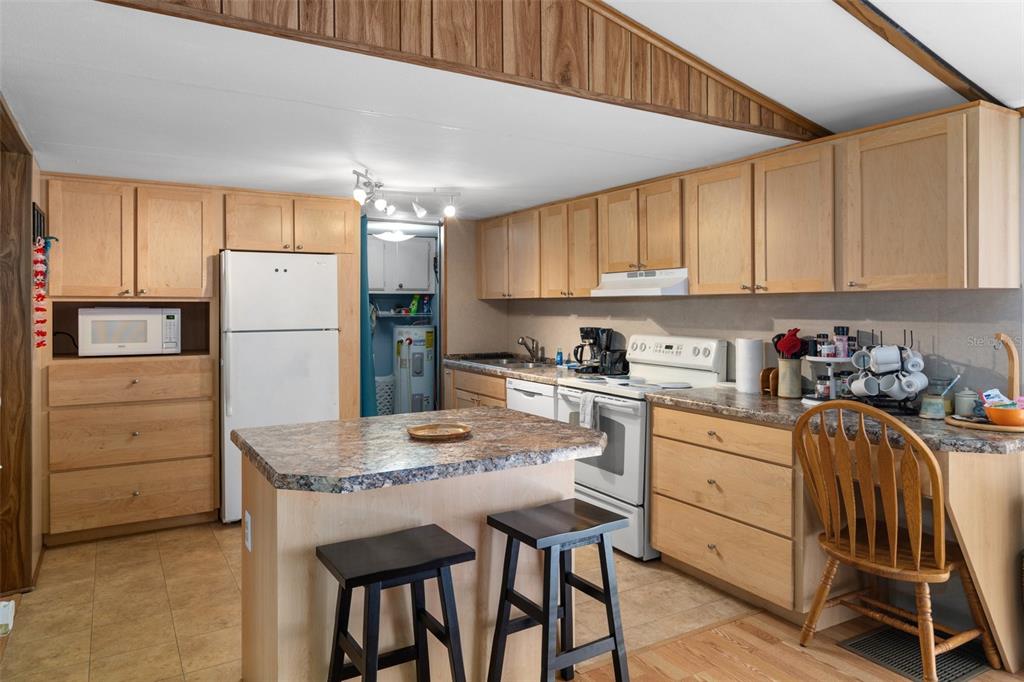 A kitchen features light wood cabinets, a center island with two stools, and white appliances — 7510 W OTTER STREET, HOMOSASSA, FL