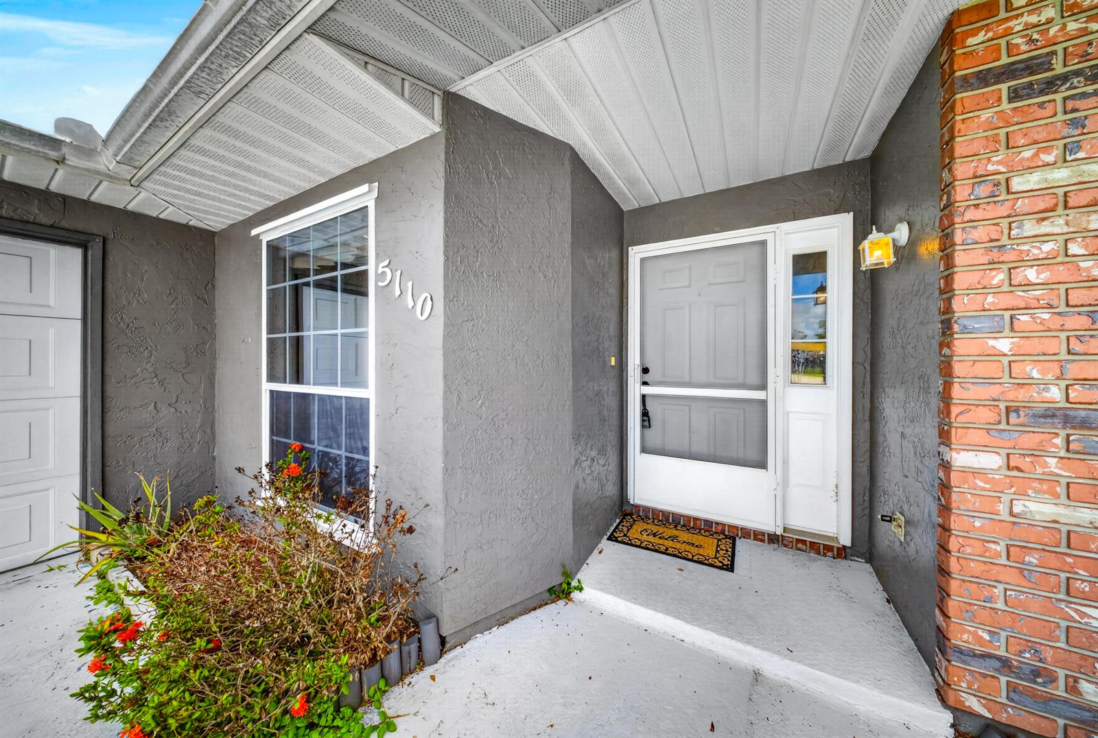 The exterior of a home features a gray stucco wall, a front door, and brick accents — 5110 Eagle Drive, Fort Pierce FL 34951, FORT PIERCE, FL