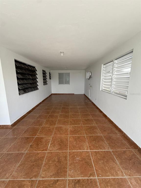 An empty, long room with brown tiled floors, white walls, and several louvered windows — PR 156 Quebrada Grande QUEBRADA GRANDE, BARRANQUITAS, PR