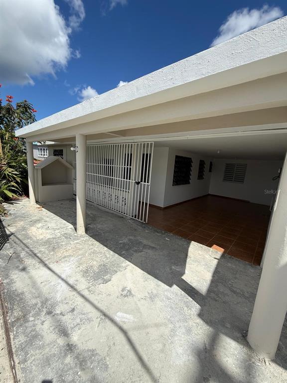 A covered concrete patio features a white metal security gate and tiled flooring — PR 156 Quebrada Grande QUEBRADA GRANDE, BARRANQUITAS, PR
