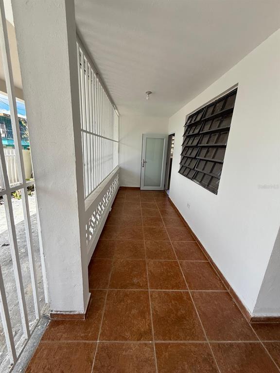 A covered outdoor porch with brown tile flooring, white walls, and a metal security gate — PR 156 Quebrada Grande QUEBRADA GRANDE, BARRANQUITAS, PR