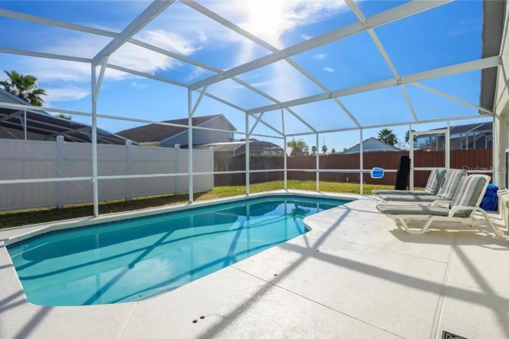 A swimming pool with a white screen enclosure and lounge chairs on a concrete patio — 160 BLOOMINGDALE DRIVE, DAVENPORT, FL