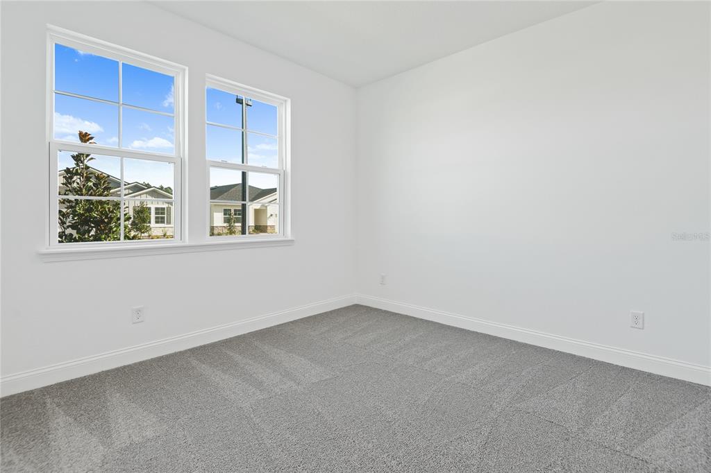 An empty bedroom features white walls, gray carpeting, and two windows overlooking a neighborhood — 200 ENCLAVE AVENUE, PALM COAST, FL