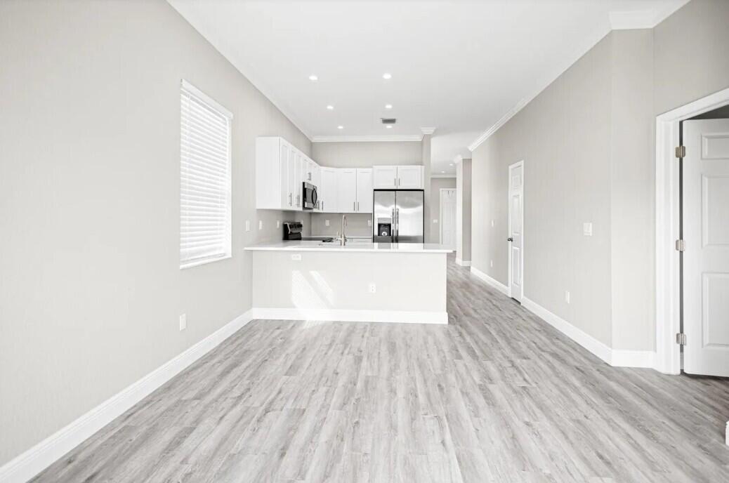 A modern kitchen with white cabinets and stainless steel appliances overlooks a light-floored living area — 132 NW 11th Avenue, Boynton Beach FL 33435, BOYNTON BEACH, FL