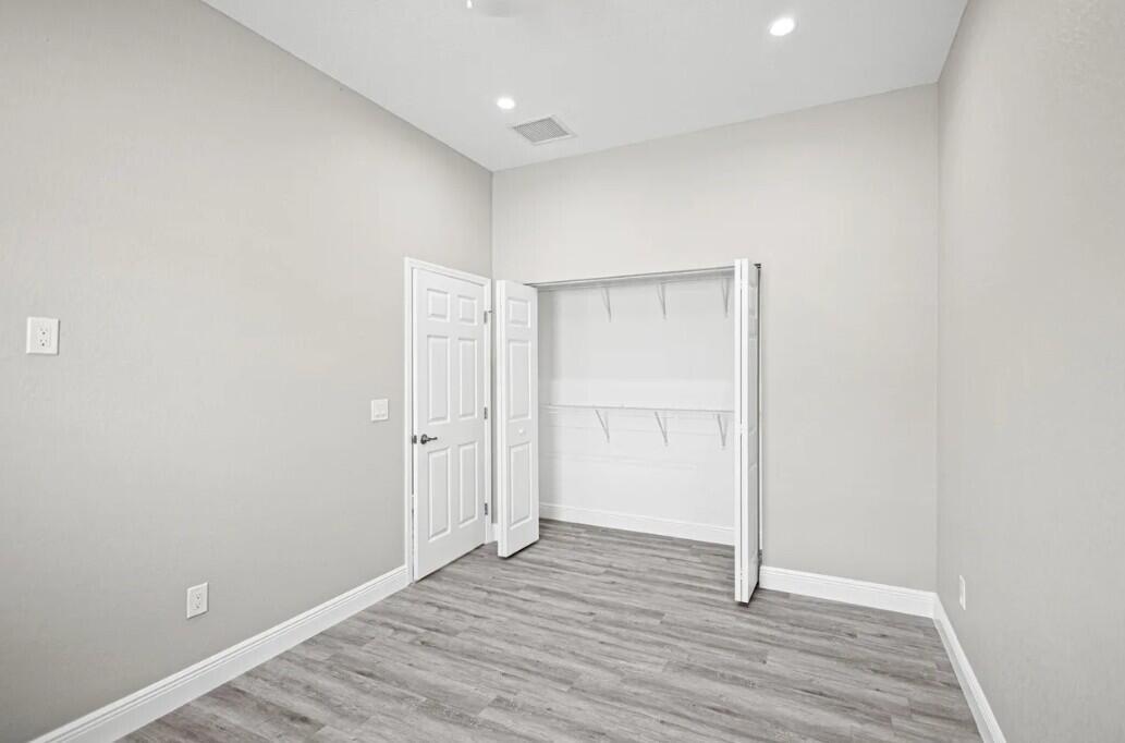 An empty room with light gray walls, wood-look flooring, a closet, and a white door — 132 NW 11th Avenue, Boynton Beach FL 33435, BOYNTON BEACH, FL