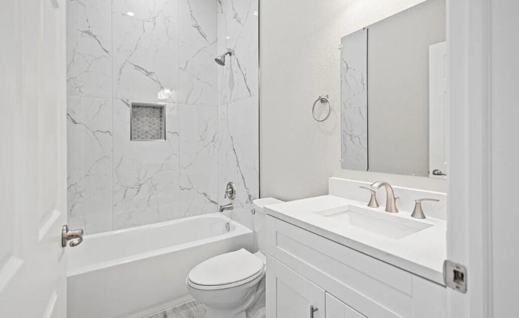 A bathroom features a white vanity, a toilet, and a tub with marble-patterned tile walls — 132 NW 11th Avenue, Boynton Beach FL 33435, BOYNTON BEACH, FL