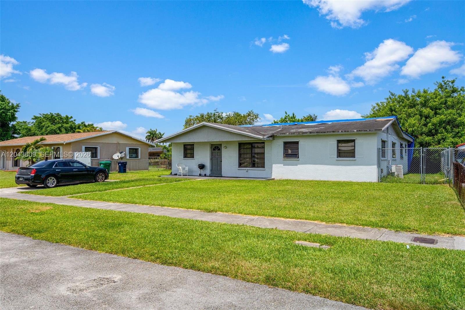 A single-story white house with a blue tarp on the roof sits on a lawn — 14125 SW 109th Pl, Miami FL 33176, MIAMI, FL