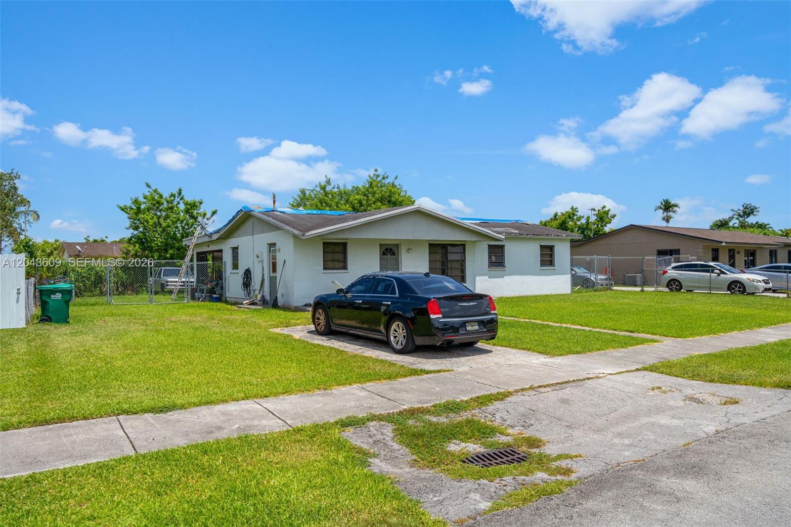 A single-story house with a blue tarp on the roof sits behind a black car — 14125 SW 109th Pl, Miami FL 33176, MIAMI, FL