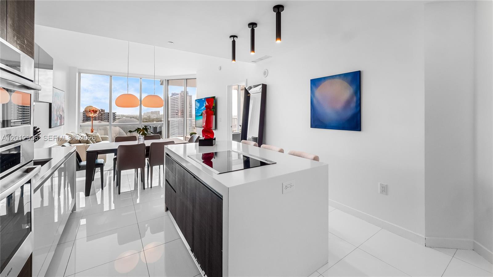 A modern kitchen features a white island with a cooktop, dark cabinetry, and dining area — 851 NE 1st Ave # 1606, Miami FL 33132, MIAMI, FL