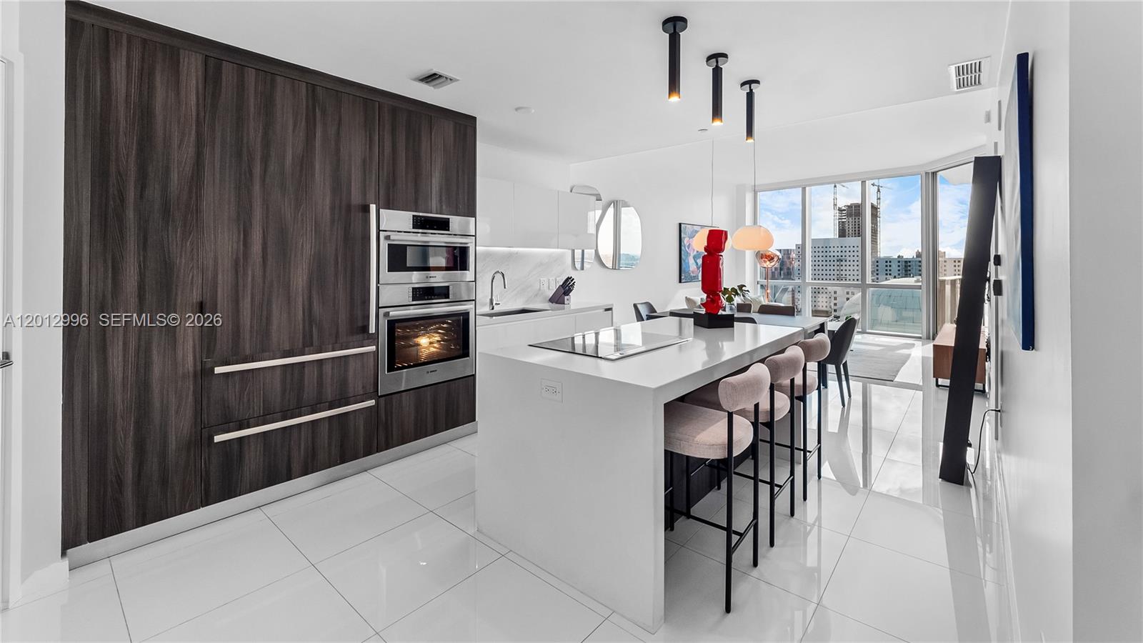 A modern kitchen features dark wood cabinetry, a white island with seating, and floor-to-ceiling windows — 851 NE 1st Ave # 1606, Miami FL 33132, MIAMI, FL