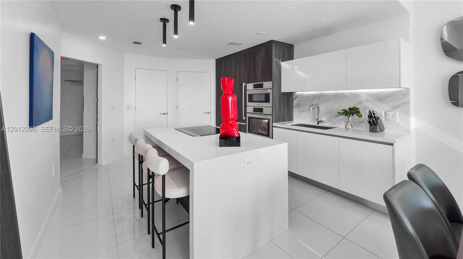 A modern kitchen features a white island, glossy cabinets, marble backsplash, and dark wood accents — 851 NE 1st Ave # 1606, Miami FL 33132, MIAMI, FL