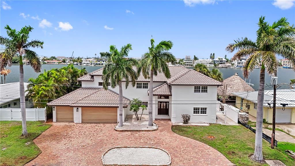 A two-story white house with a tiled roof and brick driveway sits along the water — 423 55TH AVENUE, ST PETE BEACH, FL