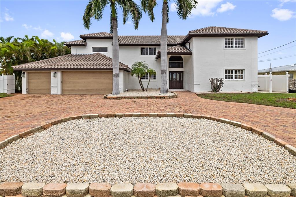 A two-story white house with a brick driveway, palm trees, and a gravel circular bed — 423 55TH AVENUE, ST PETE BEACH, FL