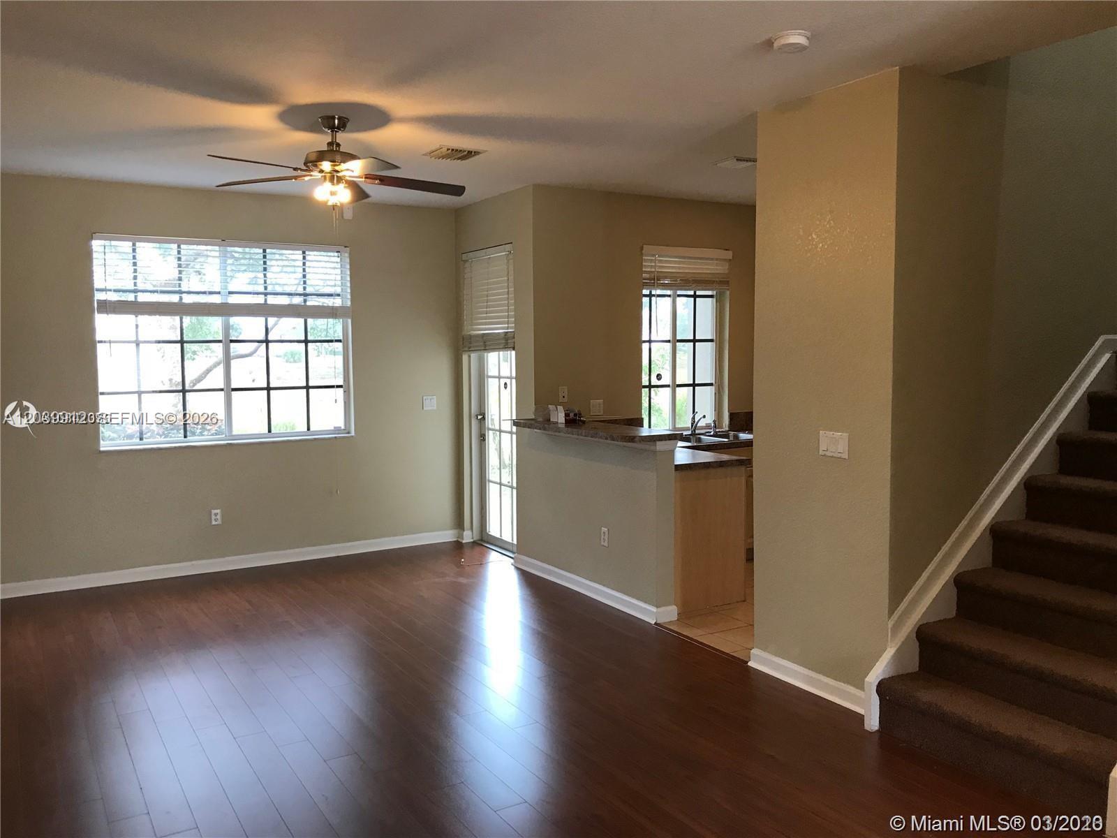 A living room with dark wood flooring, a ceiling fan, and an adjacent kitchen area — 1413 Lucaya Dr, Riviera Beach FL 33404, RIVIERA BEACH, FL
