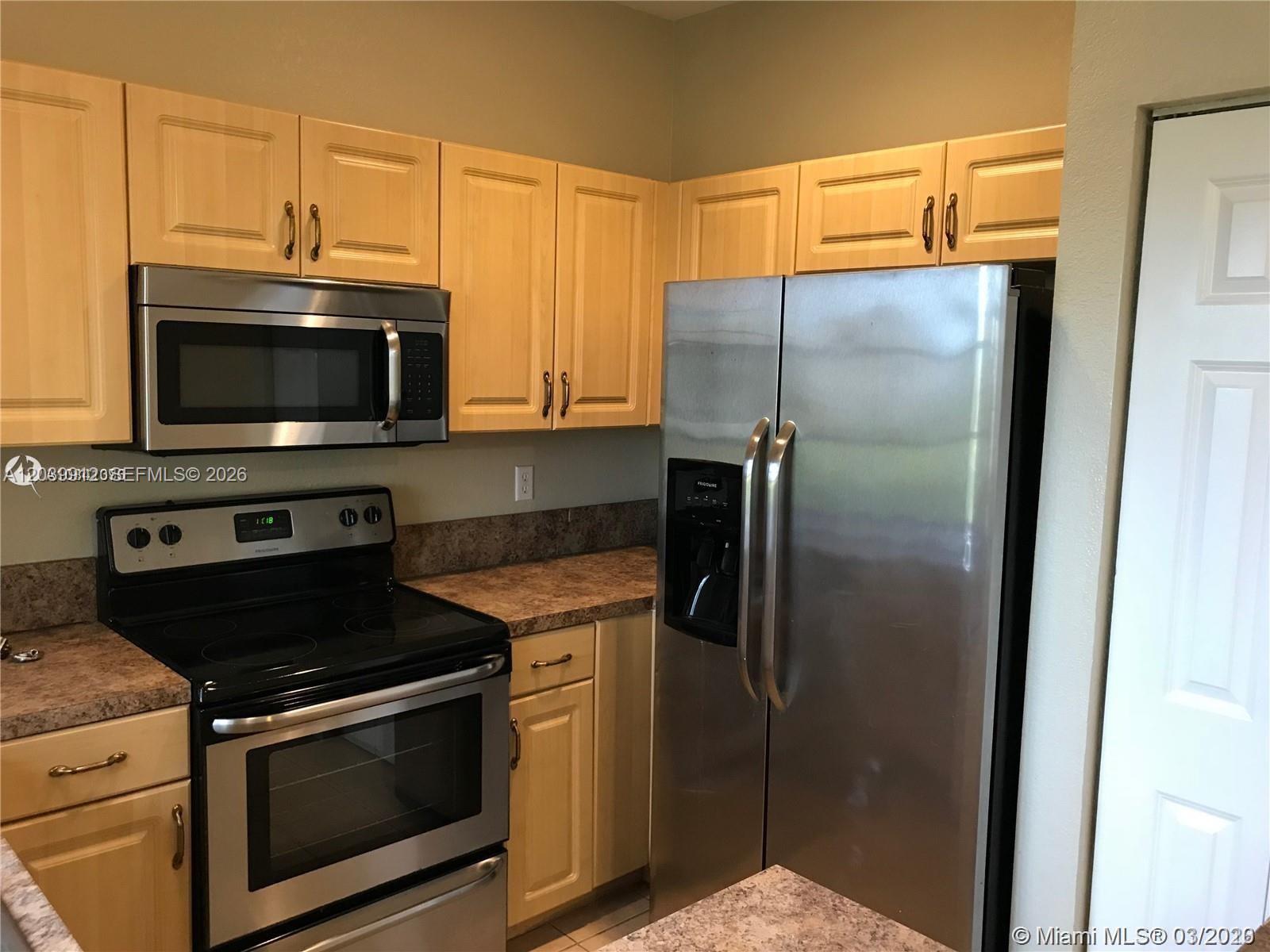 A kitchen features light wood cabinets, stainless steel appliances, and brown laminate countertops — 1413 Lucaya Dr, Riviera Beach FL 33404, RIVIERA BEACH, FL