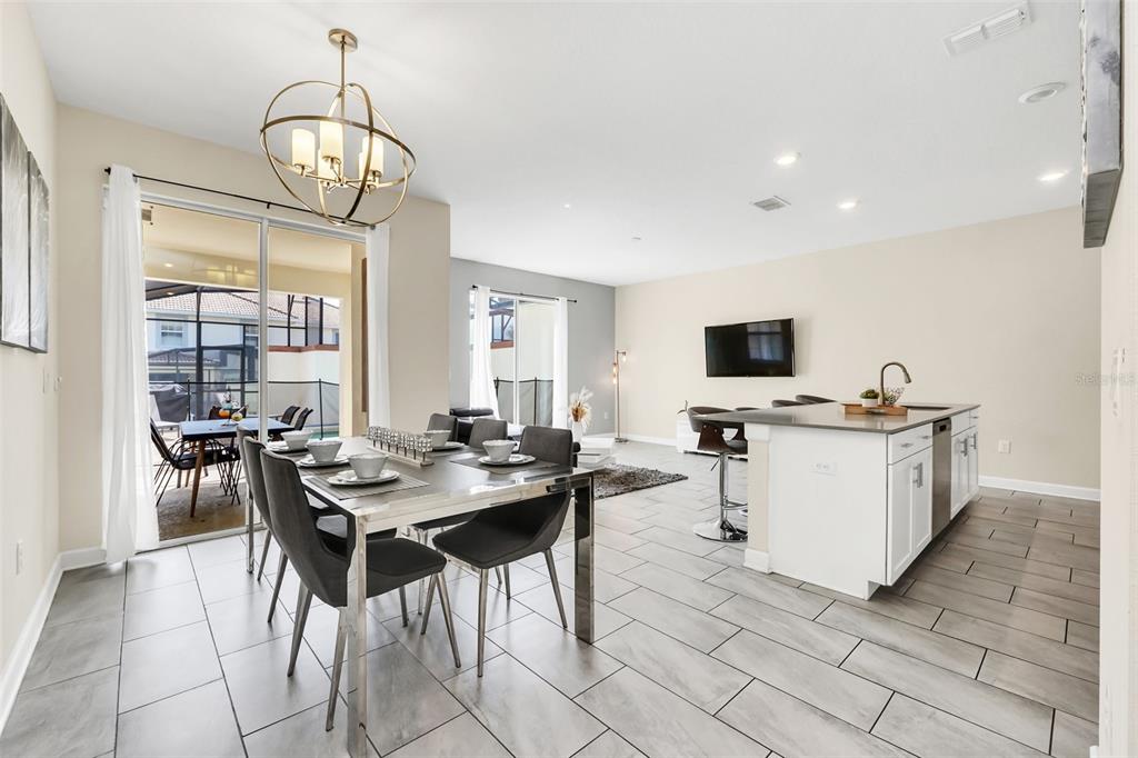 An open-concept dining area and kitchen feature gray tile flooring, white cabinetry, and sliding doors — 1571 PLUNKER DRIVE, DAVENPORT, FL