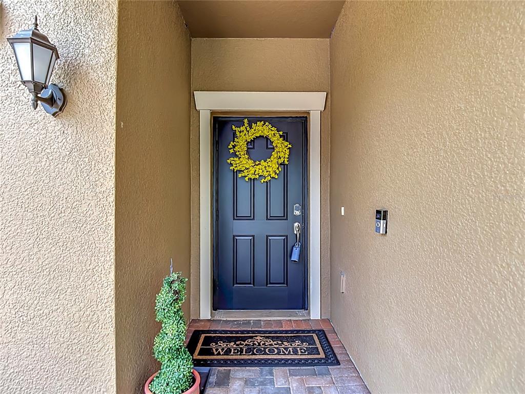 A dark front door with a yellow wreath sits under a covered entryway — 17488 TERRAZZO WAY, LAND O LAKES, FL