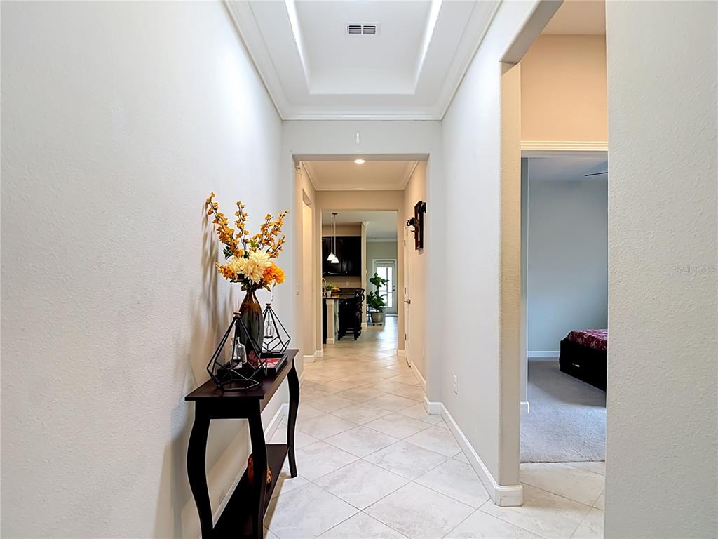 A hallway with tile flooring leads toward a kitchen, with a console table in the foreground — 17488 TERRAZZO WAY, LAND O LAKES, FL