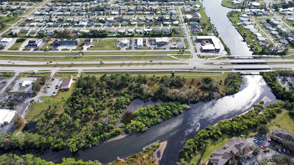 An aerial view shows a wooded lot adjacent to a river near a highway and neighborhood — 14161 S TAMIAMI TRAIL, NORTH PORT, FL