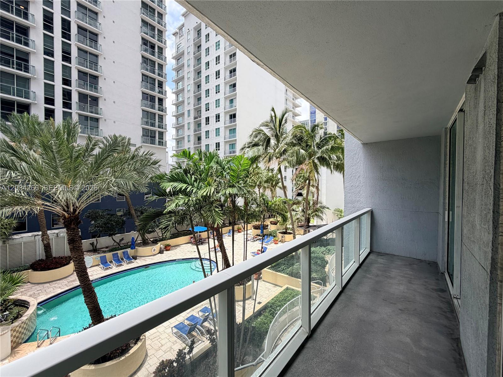 A balcony overlooks a swimming pool area surrounded by palm trees and tall apartment buildings — 253 NE 2nd St # 1006, Miami FL 33132, MIAMI, FL