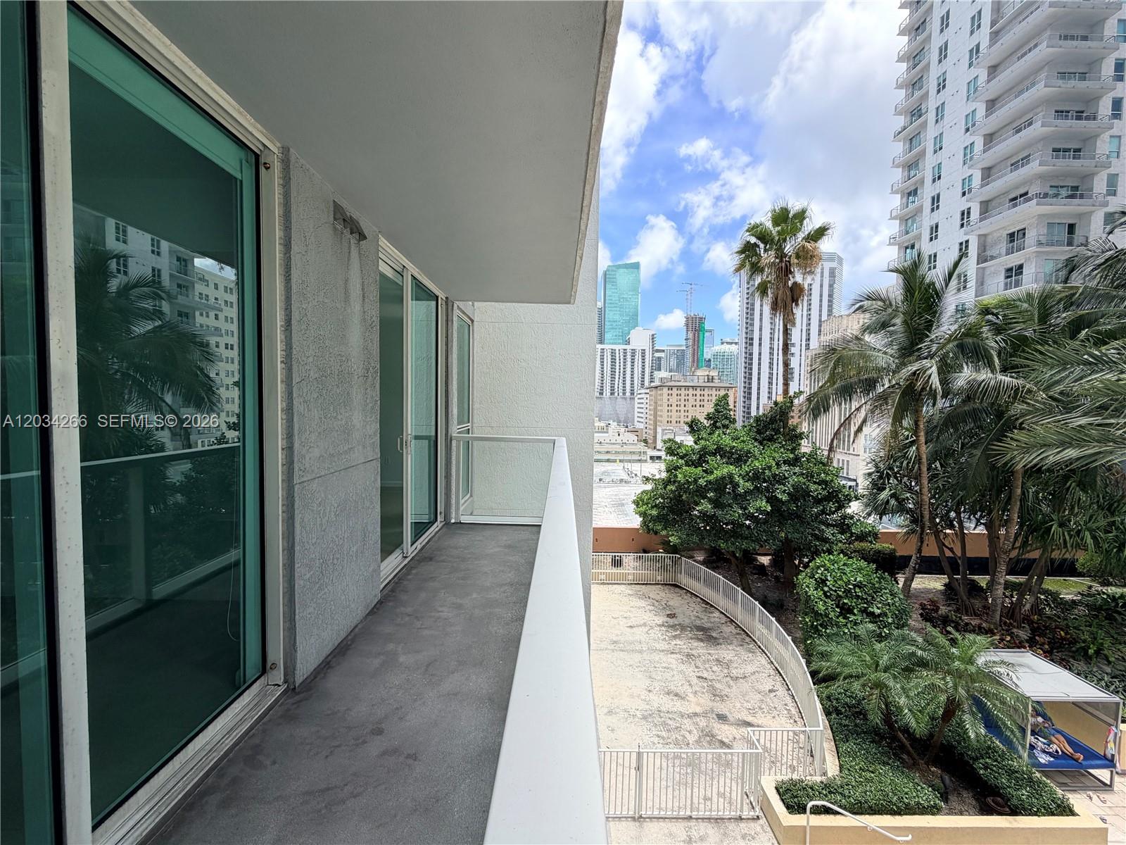 A balcony with a concrete floor and glass railing overlooks a courtyard and city skyline — 253 NE 2nd St # 1006, Miami FL 33132, MIAMI, FL