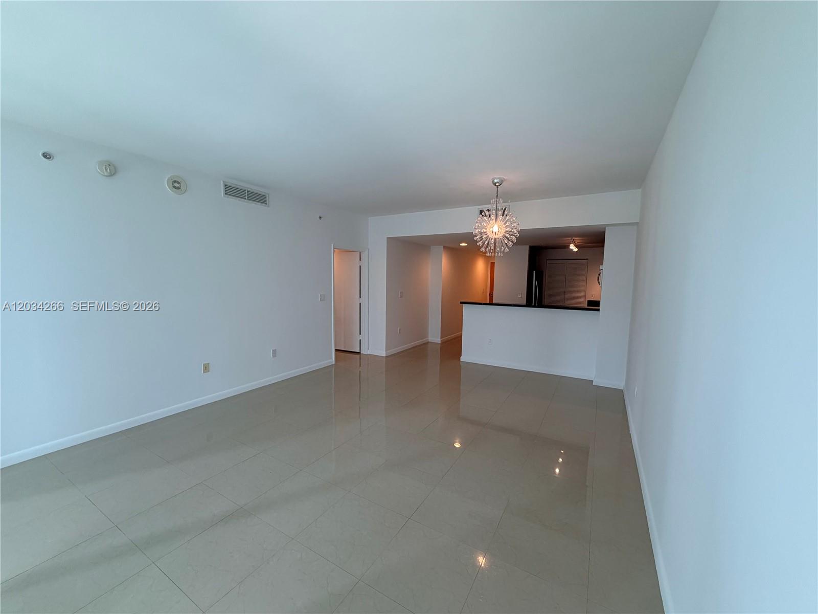 An empty living area features light-colored tile flooring, white walls, and a modern chandelier — 253 NE 2nd St # 1006, Miami FL 33132, MIAMI, FL