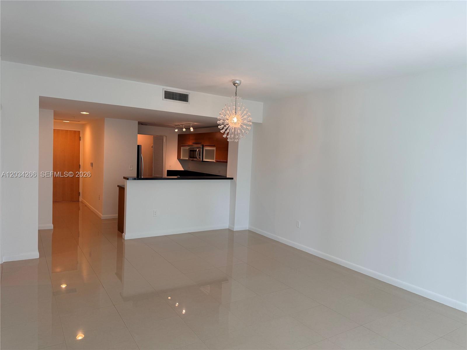 An open-concept living area features light tile flooring, a kitchen breakfast bar, and a chandelier — 253 NE 2nd St # 1006, Miami FL 33132, MIAMI, FL