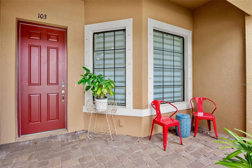 A red front door and two red chairs sit on a paved entryway porch — 5425 CICERONE STREET UNIT 103, SARASOTA, FL