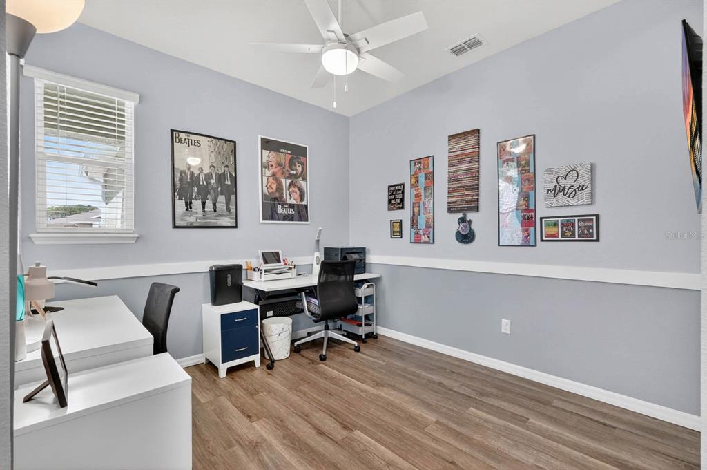 A home office features light blue walls, wood-look flooring, a ceiling fan, and music-themed wall decor — 2708 KINSALE LANE, ORMOND BEACH, FL