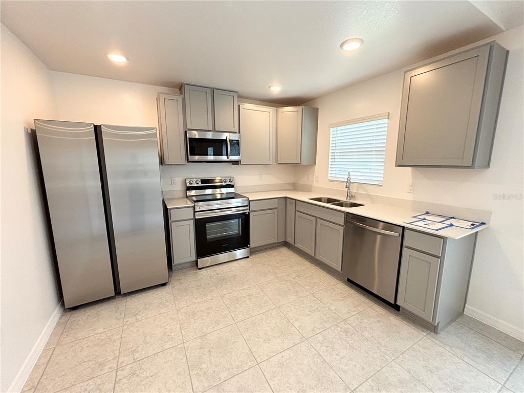 A kitchen features gray cabinets, stainless steel appliances, white countertops, and light-colored tile flooring — 137 MAPLE DRIVE W, KISSIMMEE, FL
