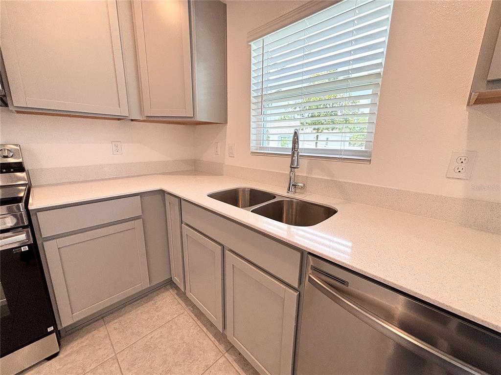 A kitchen features light gray cabinets, white quartz countertops, a stainless steel sink, and appliances — 137 MAPLE DRIVE W, KISSIMMEE, FL