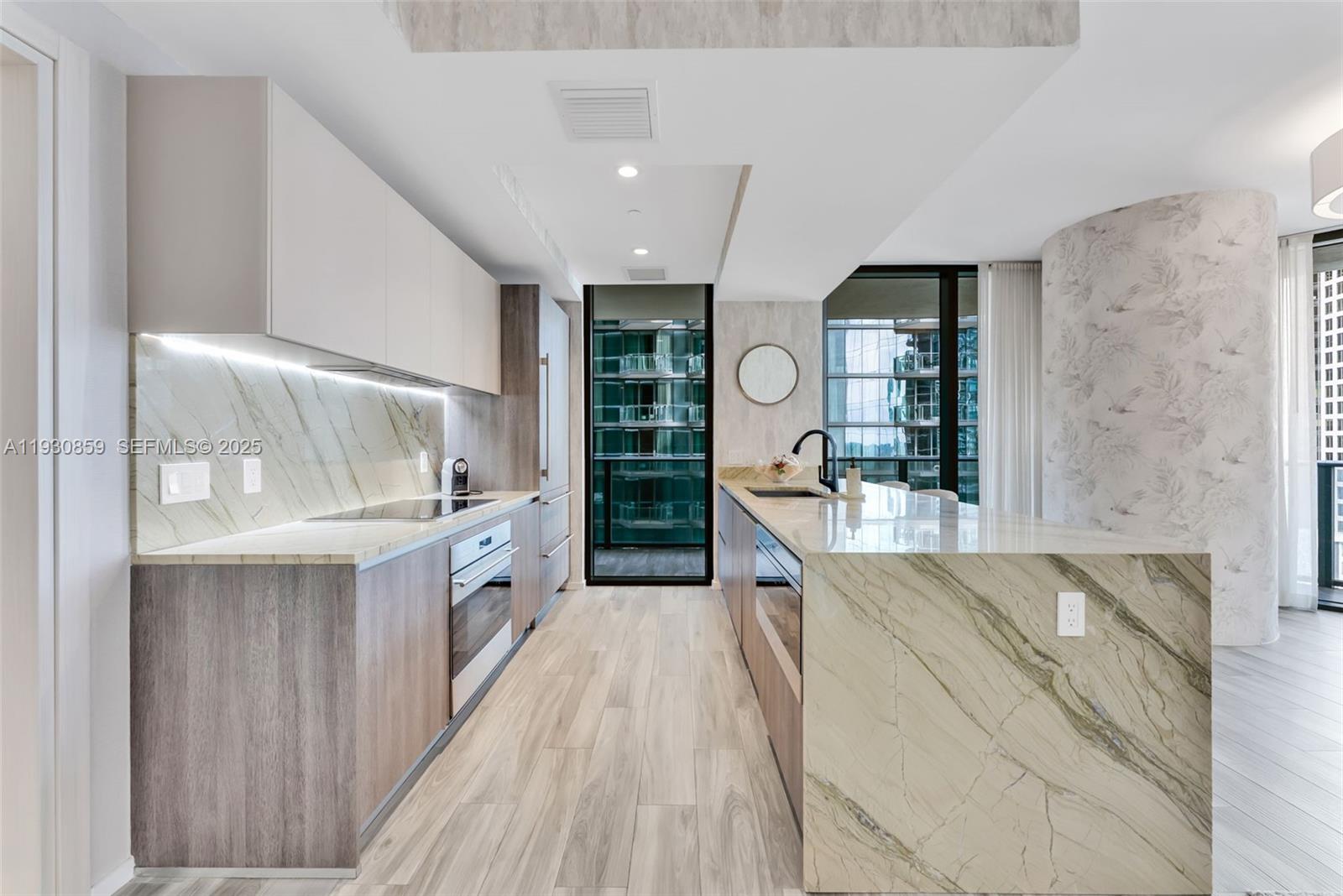 A modern kitchen features wood-toned cabinetry, marble countertops, and a large central island — 801 S Miami Ave # 1805, Miami FL 33130, MIAMI, FL