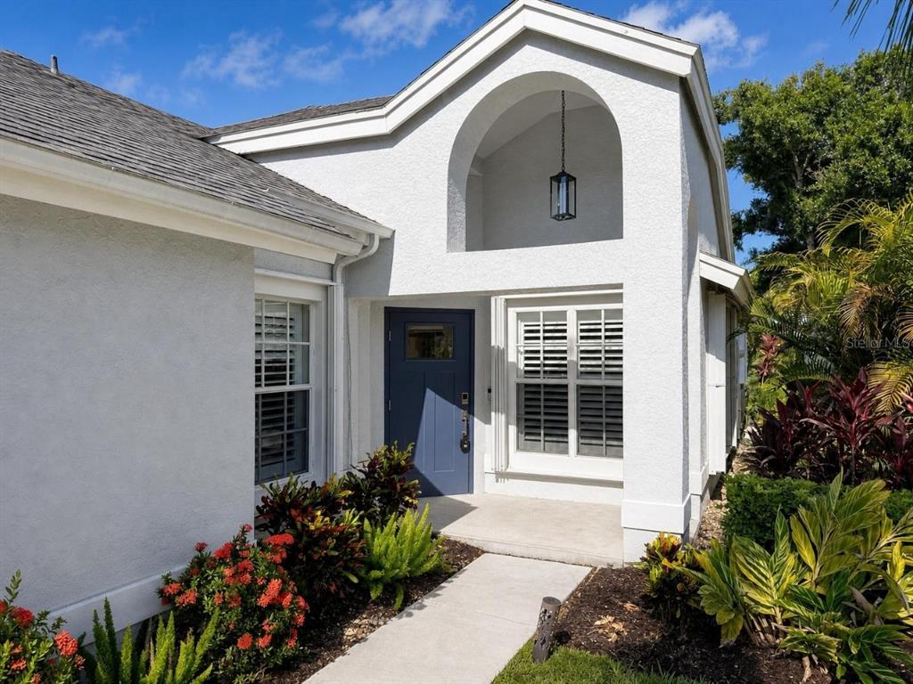 The exterior of a white house features a blue front door and an arched entryway — 20822 COUNTRY BARN DRIVE, ESTERO, FL
