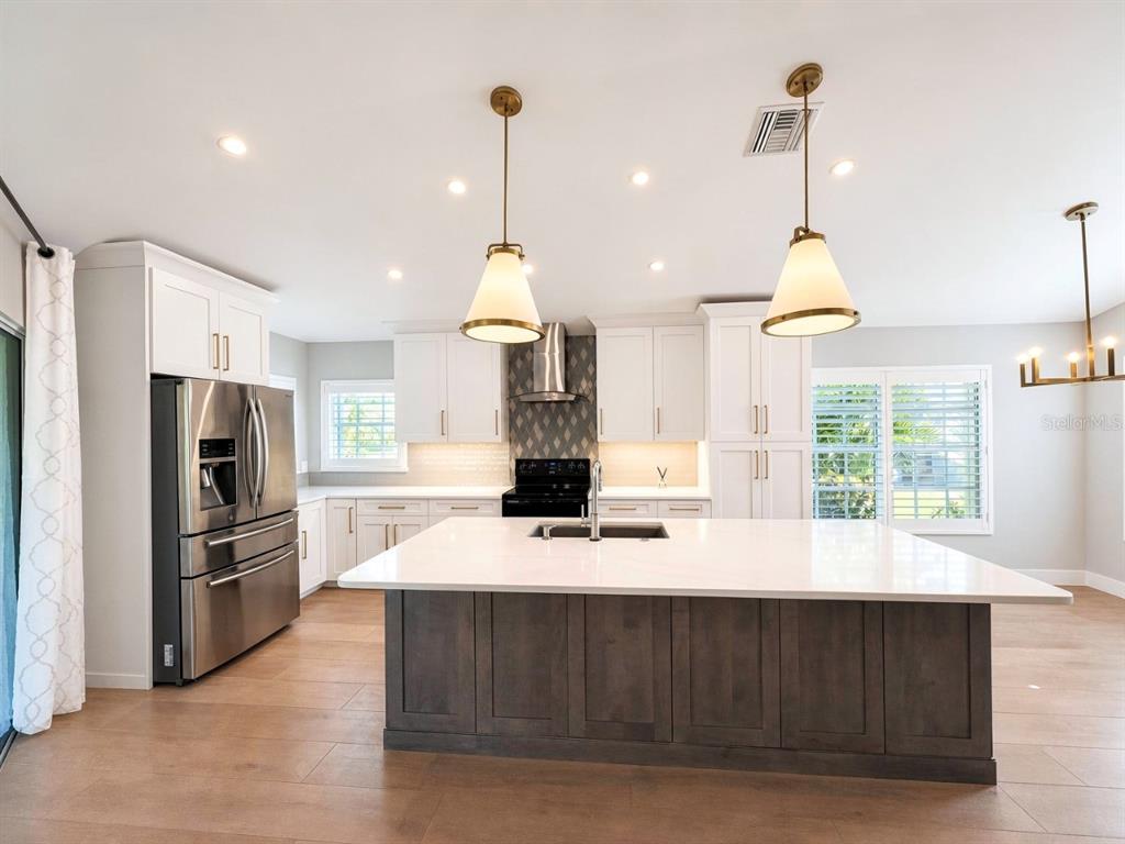 A modern kitchen features white cabinetry, a dark wood island with a sink, and stainless appliances — 20822 COUNTRY BARN DRIVE, ESTERO, FL