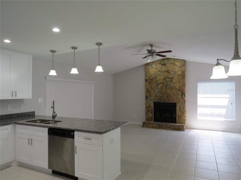 A kitchen with granite countertops and white cabinets opens into a living room with fireplace — 4023 PADDLEWHEEL DRIVE, BRANDON, FL