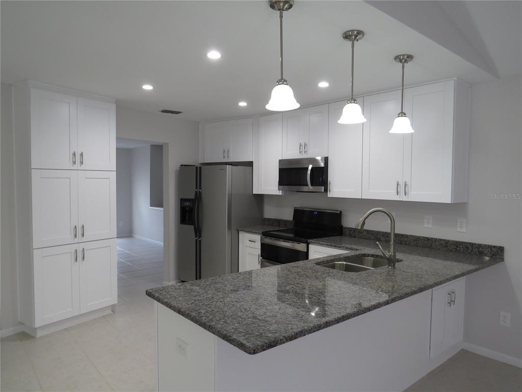 A kitchen features white cabinetry, granite countertops, stainless steel appliances, and a central island — 4023 PADDLEWHEEL DRIVE, BRANDON, FL