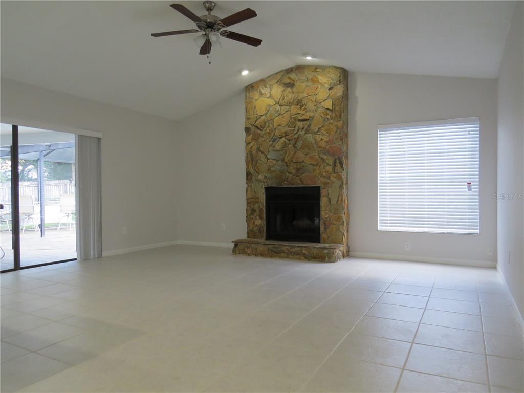 A living room features a stone fireplace, tile flooring, a ceiling fan, and sliding doors — 4023 PADDLEWHEEL DRIVE, BRANDON, FL