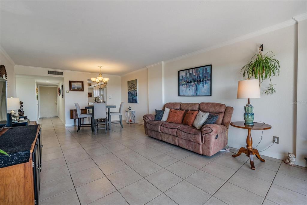 A living room with tile flooring, a brown reclining sofa, and an adjacent dining area — 2900 COVE CAY DRIVE UNIT 7B, CLEARWATER, FL