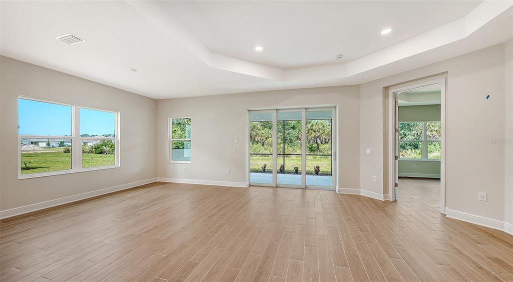 An empty room with light wood-look tile flooring, a tray ceiling, and sliding glass doors — 9940 CRYSTAL ISLES CIRCLE, SARASOTA, FL