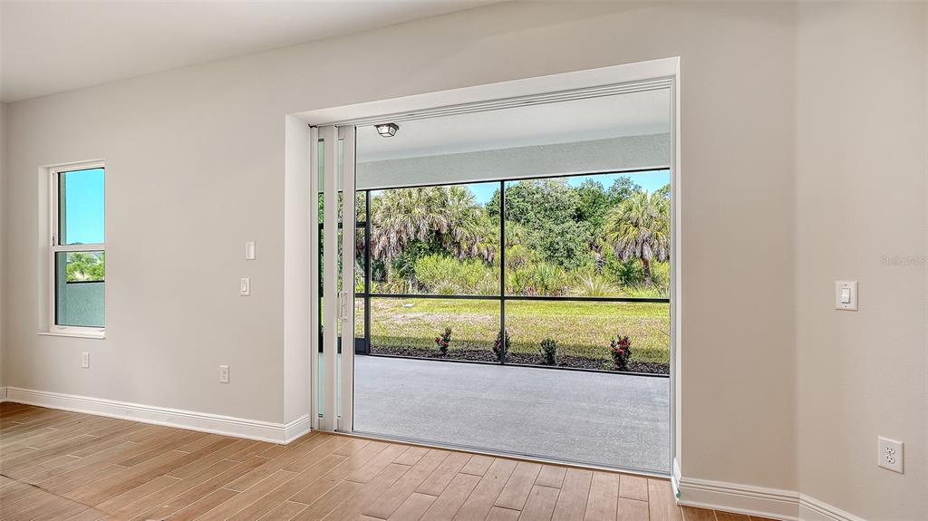 A room with wood-look tile flooring features a large sliding glass door opening to a lanai — 9940 CRYSTAL ISLES CIRCLE, SARASOTA, FL