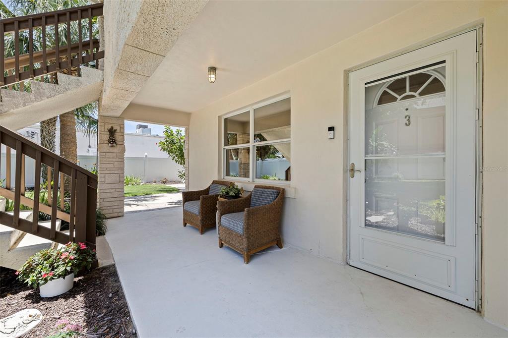 A covered porch features two wicker chairs, a white front door, and a wooden staircase — 109 16TH AVENUE UNIT 3, INDIAN ROCKS BEACH, FL