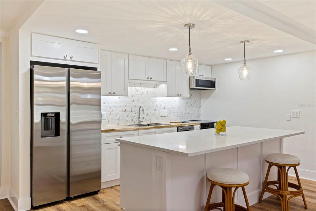 A modern kitchen features white cabinetry, stainless steel appliances, a marble backsplash, and a central island — 109 16TH AVENUE UNIT 3, INDIAN ROCKS BEACH, FL