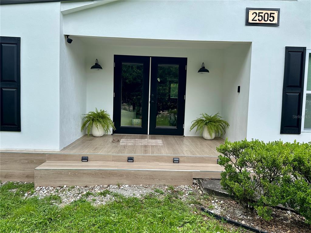 A white house exterior features a covered porch with wood-look tile, black double doors, and planters — 2505 NE 13TH AVENUE, OCALA, FL