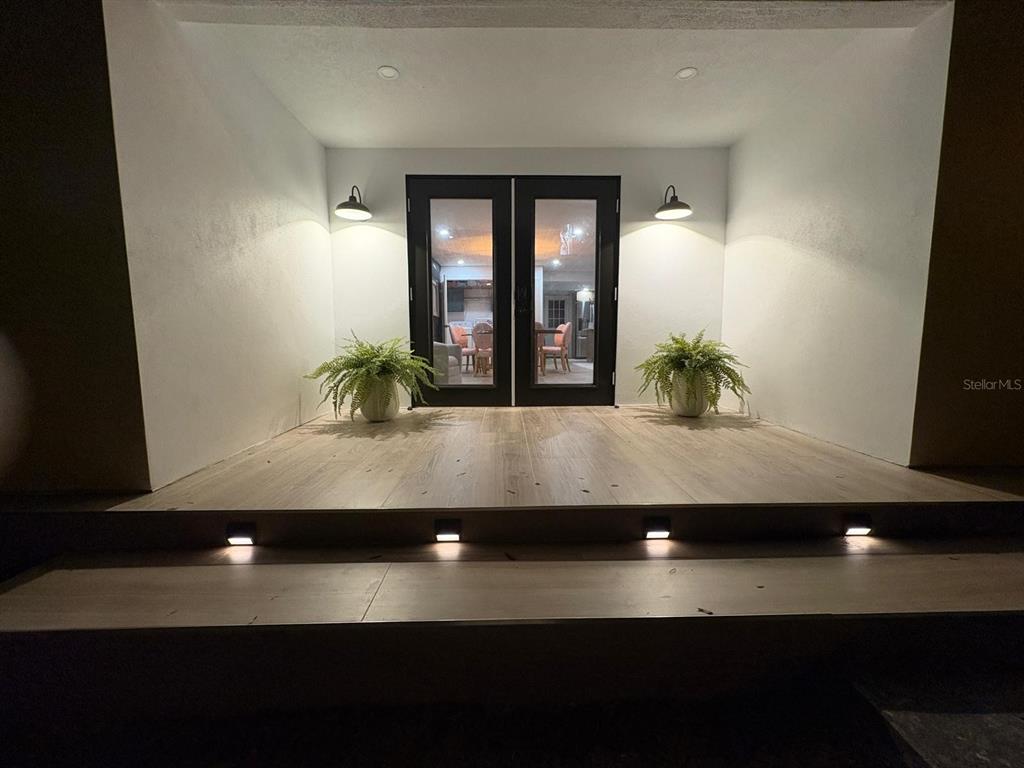 An illuminated porch with wood-look flooring, two potted ferns, and black double glass doors — 2505 NE 13TH AVENUE, OCALA, FL
