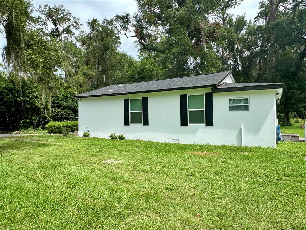 The exterior side of a white house features two windows with black shutters and a roof — 2505 NE 13TH AVENUE, OCALA, FL