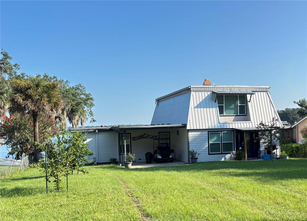 A two-story house with a gambrel roof and a carport sits on a grassy lot — 120 LITTLE ORANGE LAKE DRIVE, HAWTHORNE, FL