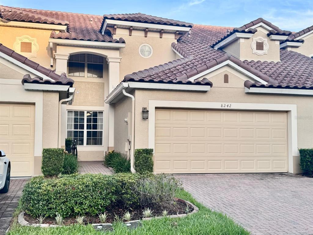 A two-story townhouse exterior features a beige stucco facade, a tiled roof, and a garage — 8242 VIA VERONA, ORLANDO, FL