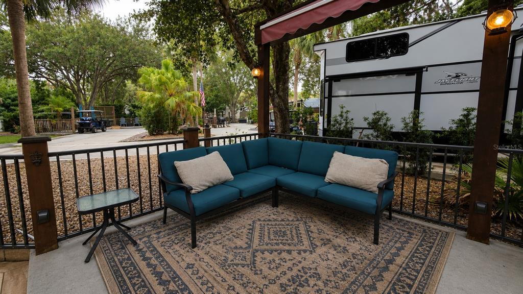 A patio features a teal sectional sofa, a small glass table, and a patterned rug — 145 HORSESHOE BEND, RIVER RANCH, FL