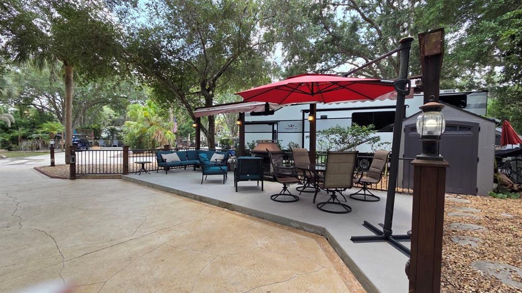 A concrete patio features outdoor furniture, a red umbrella, and a parked recreational vehicle — 145 HORSESHOE BEND, RIVER RANCH, FL