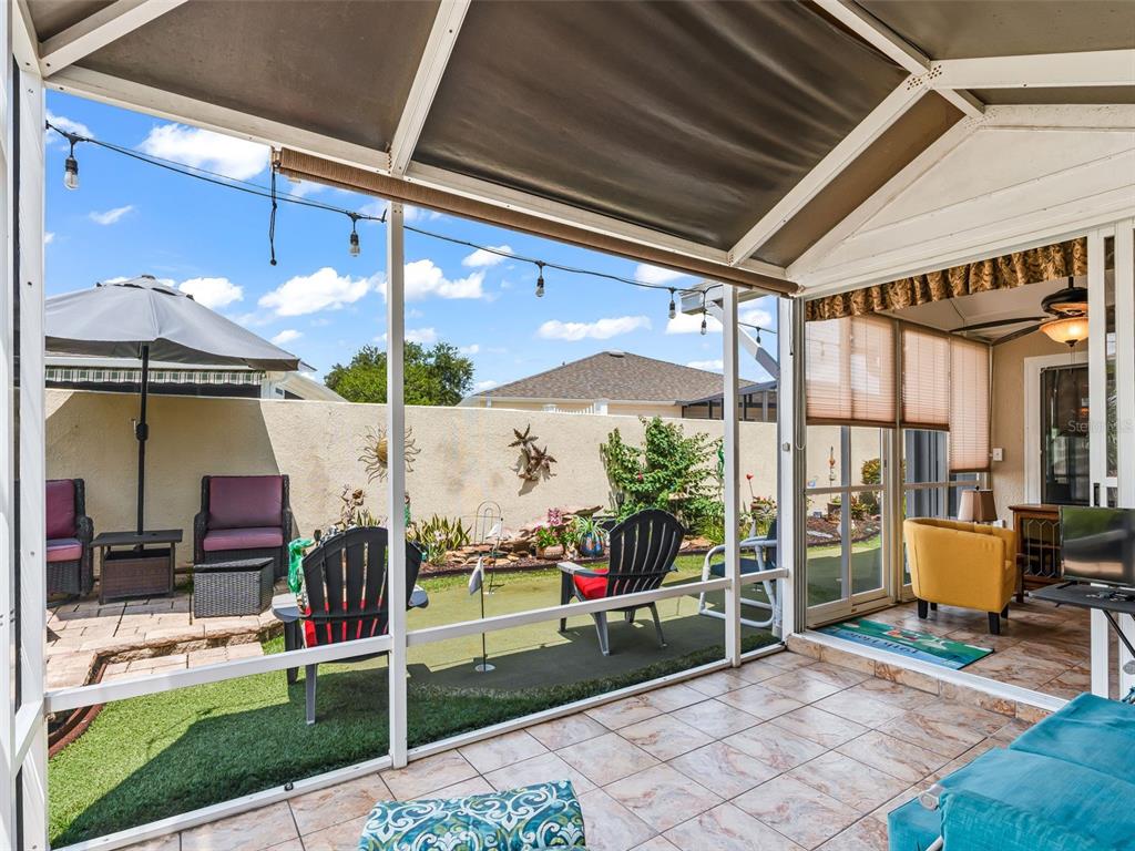 A screened-in patio features tiled flooring, outdoor seating, and a small backyard putting green — 17770 SE 85TH ELLERBE AVENUE, THE VILLAGES, FL